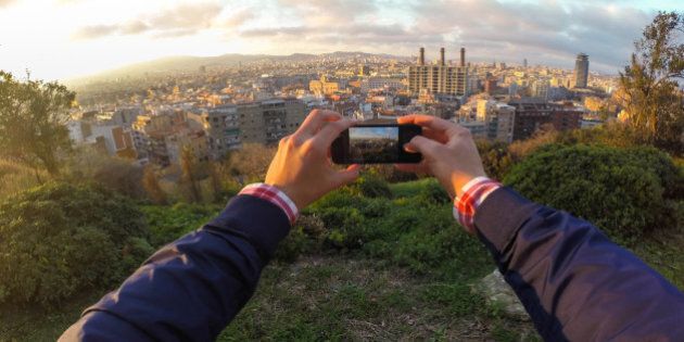 Guy taking pictures with his smartphone over the Barcelona city from mountain viewpoint and taken from personal point of view. Catalonia, Europe.