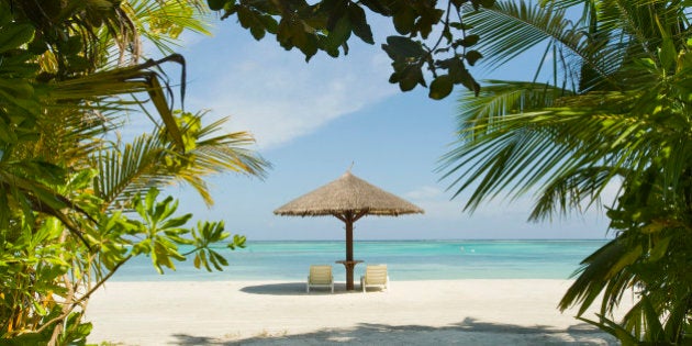 Lounge chairs and a palapa umbrella on the beach at an island resort in South Male Atoll, Maldives.