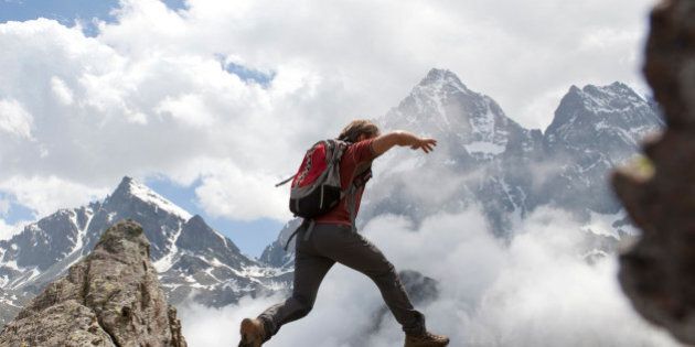 Hiker jumps across rock gap, mountains behind