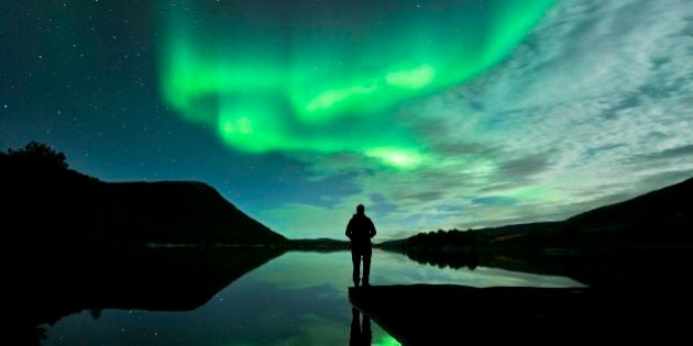 Aurora borealis. Person watching the aurora borealis (northern lights). The aurora borealis is a coloured light display that is visible in the night sky at high latitudes. It occurs when charged and energetic particles from the Sun (the solar wind) are drawn by Earths magnetic field to the polar regions. Hundreds of kilometres up, they collide with gas molecules and atoms, causing them to emit light. Photographed in Hamaroy, Nordland, Norway, in October.