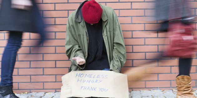 Homeless man sitting on a street passed by people