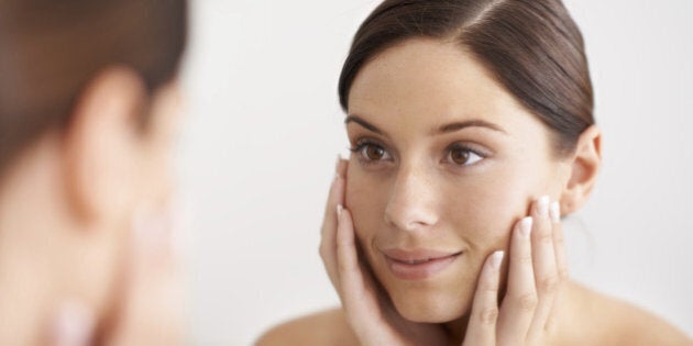 A gorgeous young woman looking at her reflection in the mirror with her hands on her face