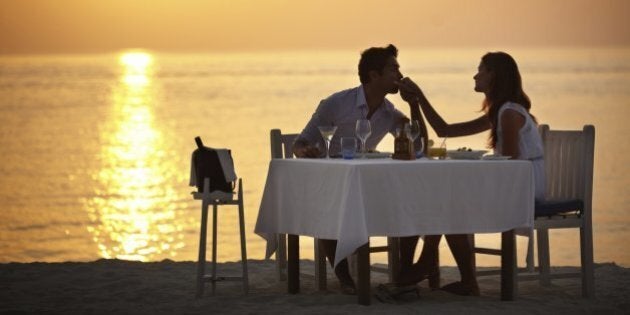 A young man kissing the hand of his wife while having dinner on the beach