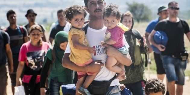 A man carries two children as he walks with other migrants near the southern Serbian village of Miratovac, travelling on foot from Macedonia to Presevo in Serbia, on August 25, 2015. At least 2,000 more migrants flooded overnight into Serbia in a desperate journey to try and go on to Hungary, the door into the European Union, a UN official said on August 24. More than 9,000 people, mostly Syrian refugees, have arrived to Serbia those last three days. AFP PHOTO / ARMEND NIMANI (Photo credit should read ARMEND NIMANI/AFP/Getty Images)