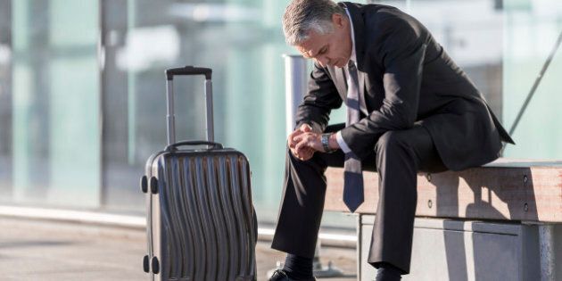Exhausted businessman with baggage sitting outside airport building