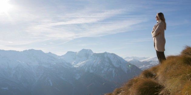 Woman stands in high mountain meadow, looking out