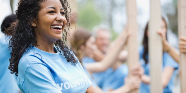 Cheerful teenage girl with volunteers building wooden frame in background