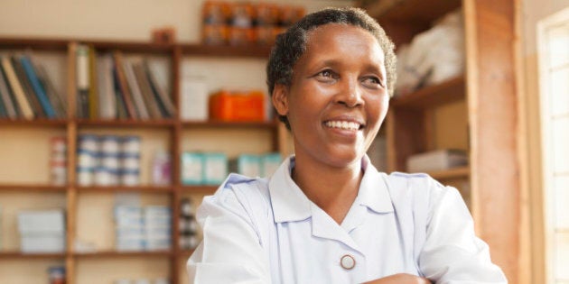 A nurse of East African descent stands proudly in a hospital with medical supplies in the background.