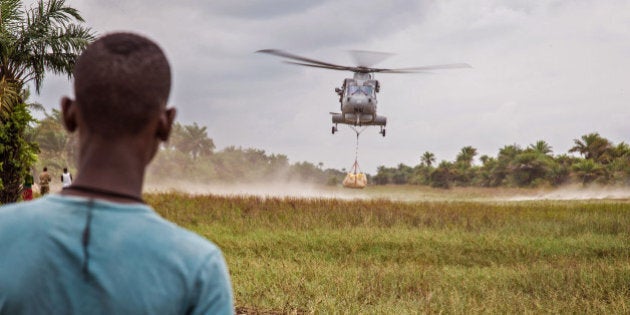 A local resident awaits the landing of a British Navy helicopter as it drops food aid on Sherbro Island, Sierra Leone, Sunday, Dec. 7, 2014. The WFP, World Food Program and British Military took part in a three day food distribution effort to local residents on the remote Sherbro Island, where the amount of sick people due to the Ebola virus have prevented people from farming, fishing or gathering there own food. (AP Photo/Michael Duff)