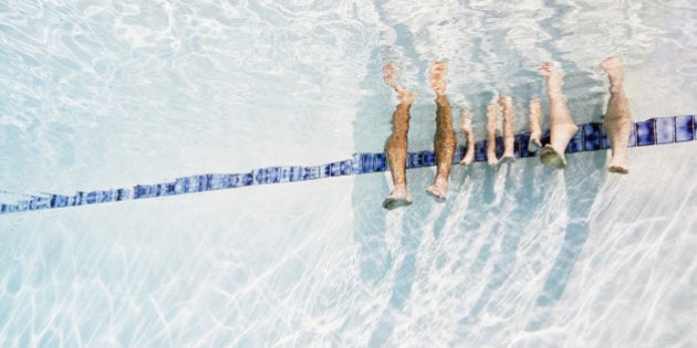 Family sitting on edge of pool resting feet in water underwater view