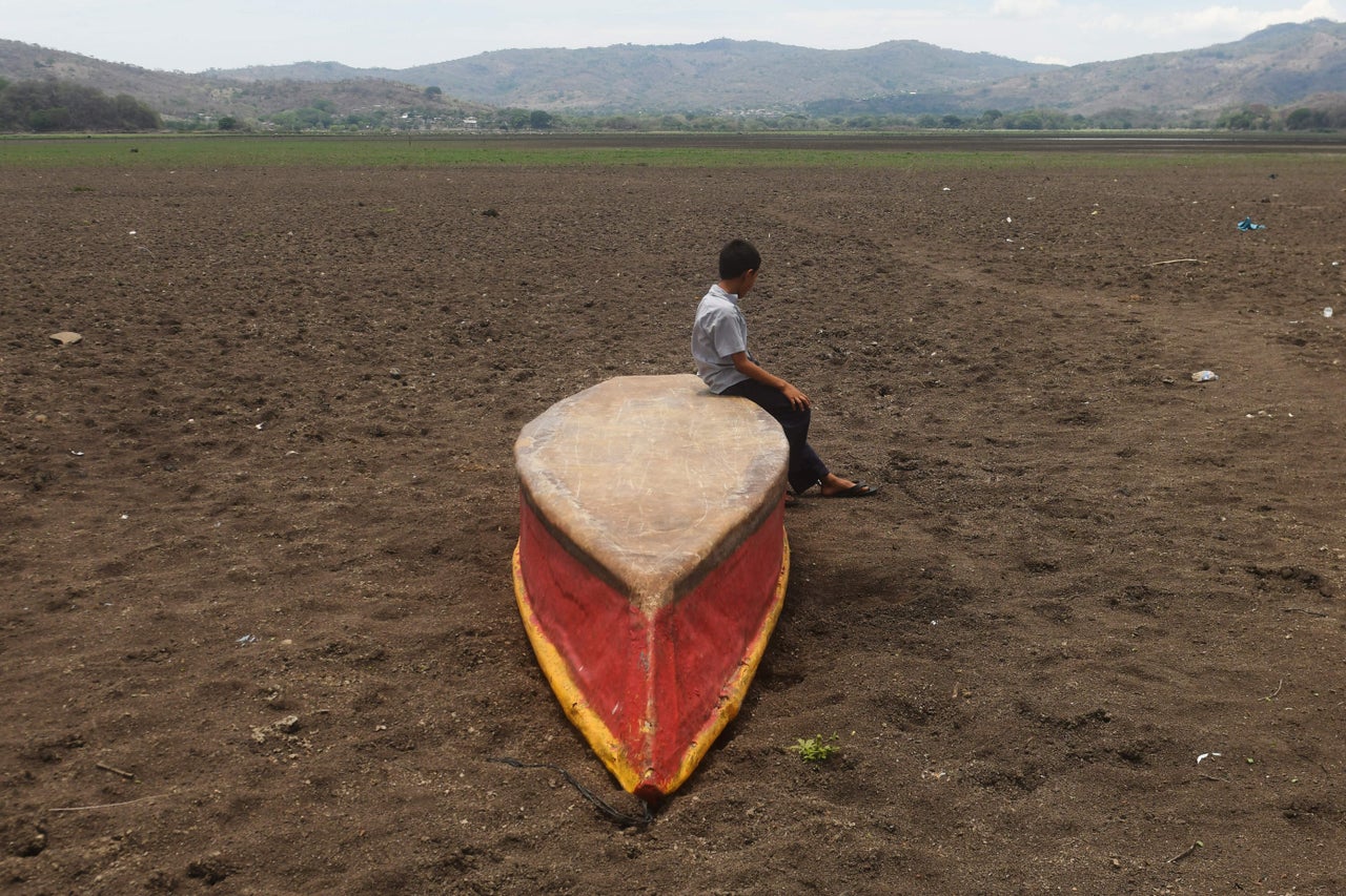 In a photo from May 2017, a boy sits on an abandoned boat on what is left of Guatemala's Lake Atescatempa, which dried up due to drought and high temperatures. 