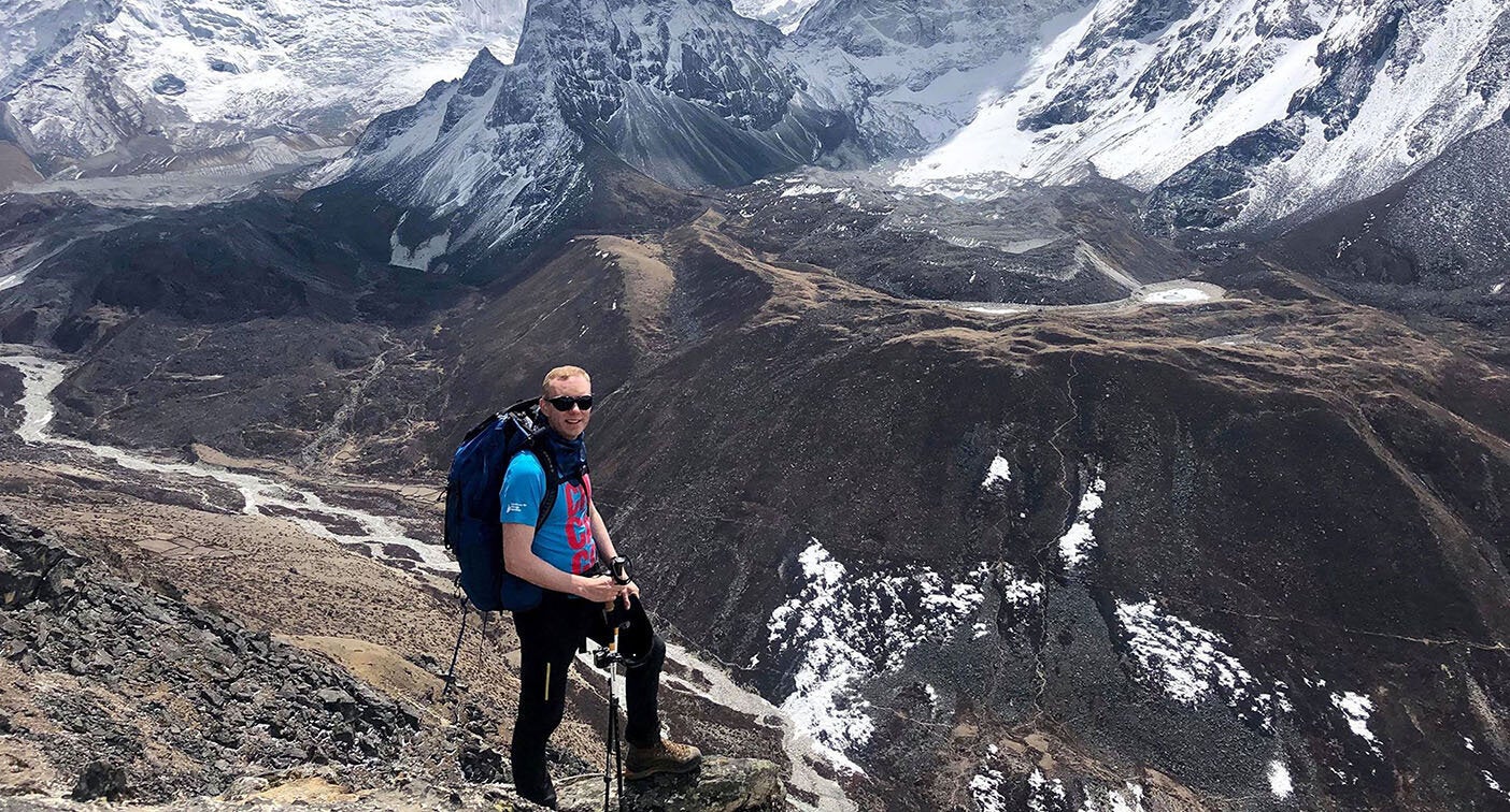 Robbie Fisher stands in front of a ravine and snowy mountain peaks.
