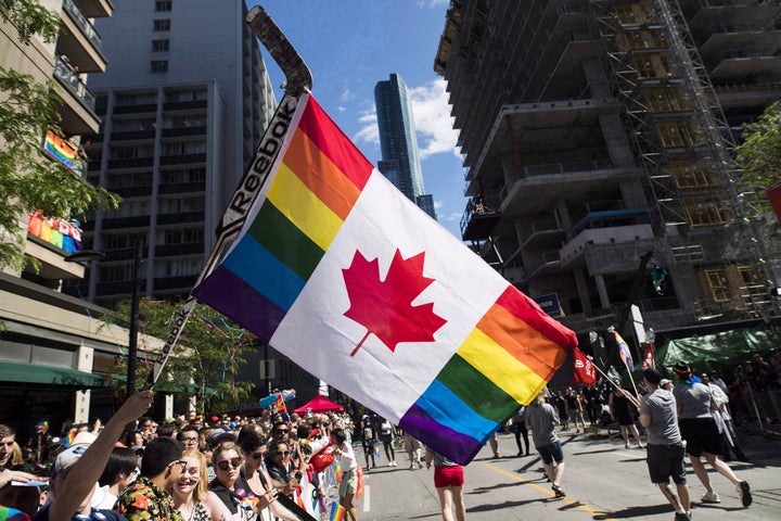 A man holds a hockey stick with a Canadian pride flag. 