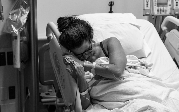 A woman clings to the side of her hospital bed after giving birth in this photo by Alex Michele