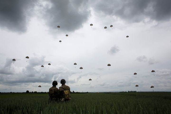 WWII enthusiasts watch French and British parachutists jumping during a commemorative parachute jump over Sannerville, Normandy.