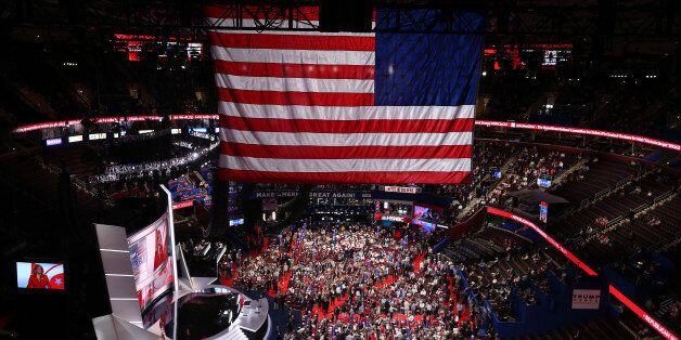 Delegates stand on the floor as an American flag hangs during the Republican National Convention (RNC) in Cleveland, Ohio, U.S., on Monday, July 18, 2016. The day before the start of the Republican National Convention in Cleveland, Reince Priebus said Donald Trump has to use the gathering to convince Americans he can be presidential. Photographer: Daniel Acker/Bloomberg via Getty Images