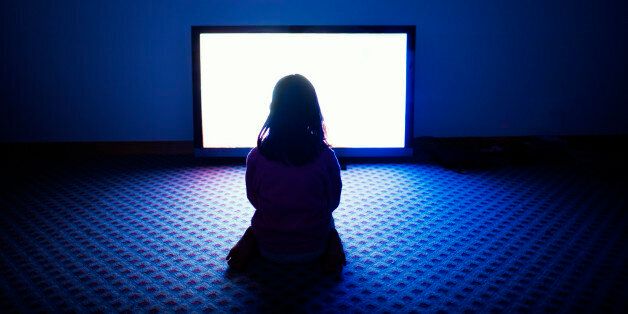 Girl sitting in front of flat screen television in dark room.