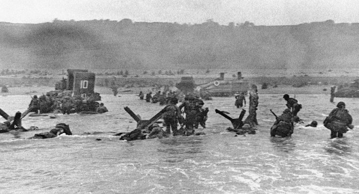 Some of the first assault troops to hit the Normandy, France beachhead on June 6, 1944 take cover behind enemy obstacles to fire on German forces as others follow the first tanks plunging through the water towards the German-held shore during World War II.