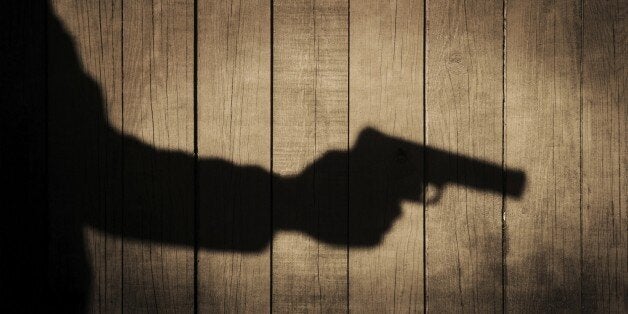 Outstretched arm with a gun. Black shadow on natural wooden background, with space for text or image.