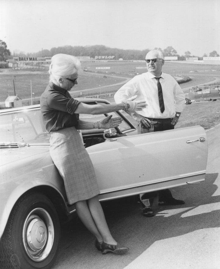 Badass racing driver Baroness Ewy von Korff-Rosqvist and Karl Kling standing next to a car as they discuss plans prior to a driving demonstration at Brand's Hatch, England, May 2, 1966. 