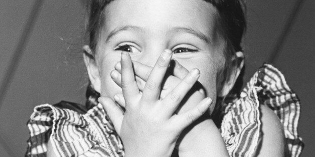 Girl (4-5) giggling, covering mouth, (B&W)