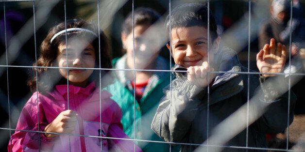 Children smile into the camera behind a fence in a temporary holding center for migrants near the border line between Serbia and Hungary in Roszke, southern Hungary in Roszke, Saturday, Sept. 12, 2015. Hundreds of thousands of Syrian refugees and others are still making their way slowly across Europe, seeking shelter where they can, taking a bus or a train where one is available, walking where it isn't. The latest string of walkers made their way Friday from the Hungarian border across Austria t