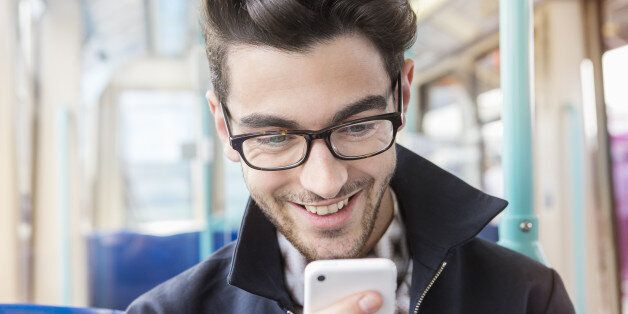man sitting in public transport looking at phone.