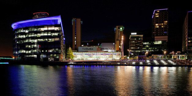 The lights of offices and restaurants are reflected in the water at MediaCityUK in Salford Quays, Manchester, U.K., on Friday, May, 29, 2015. Since the Conservatives won the general election, U.K. Chancellor of the Exchequer George Osborne announced sweeping devolution for Manchester and other English cities. Photographer: Paul Thomas/Bloomberg via Getty Images