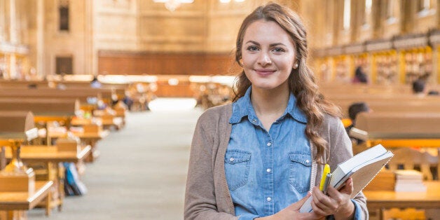 A smiling college student with books in library