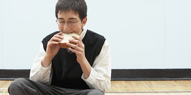 Boy (11-13) eating sandwich in school gymnasium, eyes closed