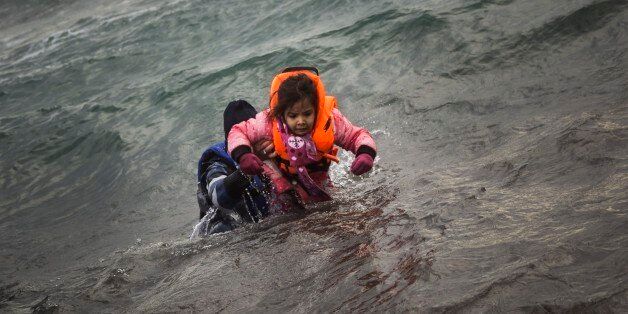 A man carries a child as they try to reach a shore after falling into the sea while disembarking from a dinghy on which they crossed a part of the Aegean sea with other refugees and migrants, from Turkey to the Greek island of Lesbos, on Sunday, Jan. 3, 2016. More than a million people reached Europe in 2015 in the continent's largest refugee influx since the end of World War II. Nearly 3,800 people are estimated to have drowned in the Mediterranean last year, making the journey to Greece or Ita
