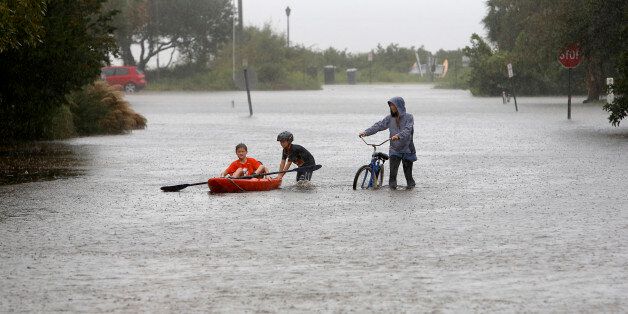 Joey Virgilio, 11, far left, sits in a kayak while his brother, Will, 9, wades in the water as mum, Kristen, pushes a bike during flood waters on Sullivan's Island, South Carolina, on Saturday