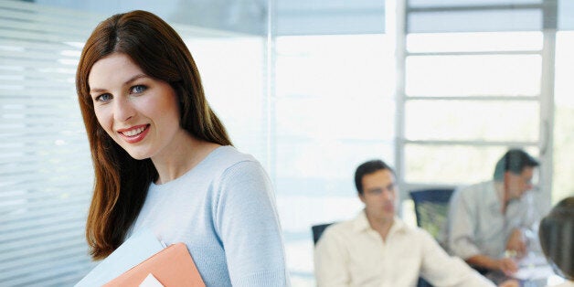 Female office worker holding papers while colleagues meet in background