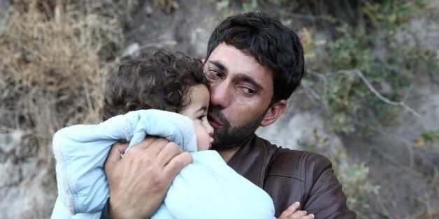 A refugee man kisses his child as they arrive by a rubber boat on the Greek island of Lesbos after crossing the Aegean sea on October 12, 2015. Refugees who begin a journey with a hope to have high living standards away from conflicts, use Greece's Lesbos Island as a transit point on their way to Europe