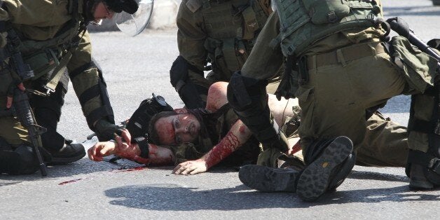 Israeli security forces tend to an injured soldier stabbed by a Palestinian man at the entrance of Hebron in the occupied West Bank on October 16, 2015. Israeli troops shot dead a Palestinian disguised as a news photographer who stabbed and wounded a soldier near the West Bank settlement of Kiryat Arba, the Israeli army said. AFP PHOTO / HAZEM BADER (Photo credit should read HAZEM BADER/AFP/Getty Images)