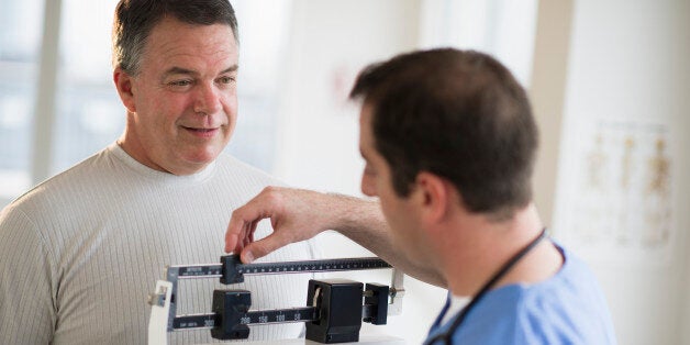 USA, New Jersey, Jersey City, Doctor assisting male patient on weighing scales in hospital