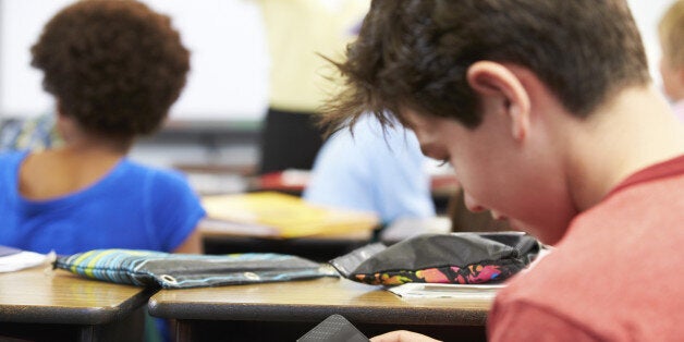 Pupil Sending Text Message On Mobile Phone In Class Sitting At Desk