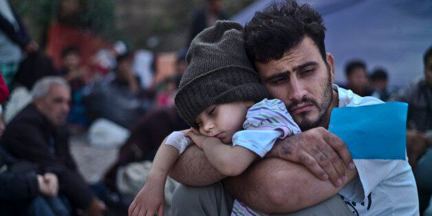 A Syrian refugee child sleeps on his father's arms while waiting at a resting point to board a bus