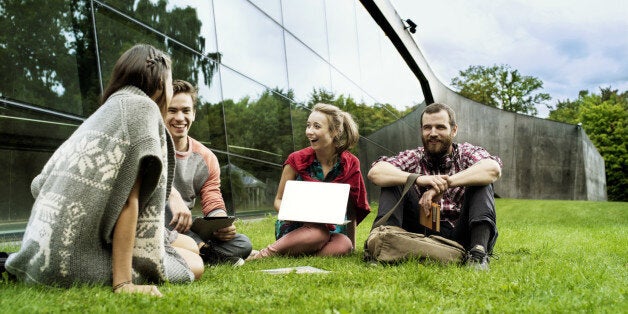 Four students sitting on the grass in front of a big modern university building