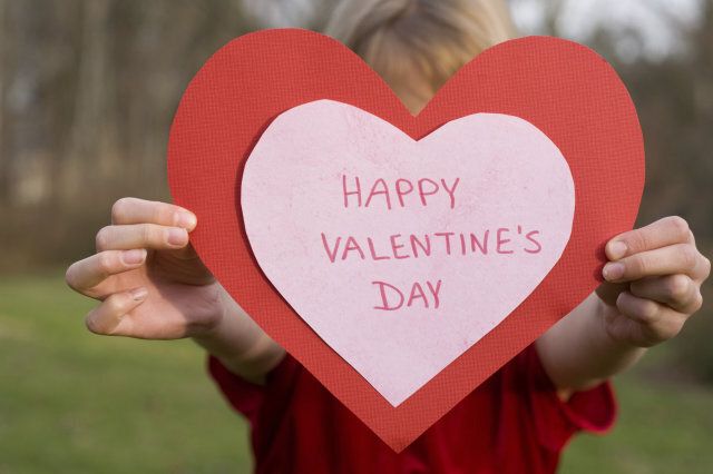 A girl holds up a very large heart shaped valentine's day card.