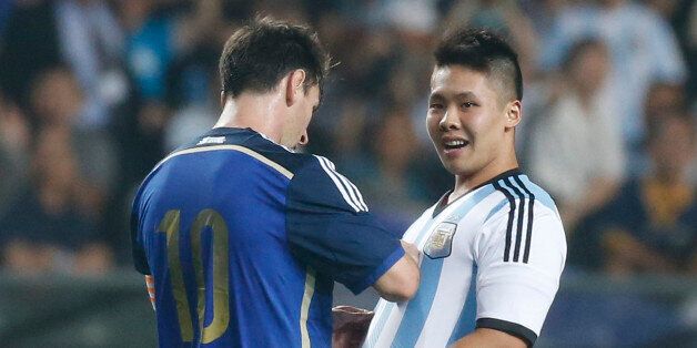 Argentina's Lionel Messi, left, signs an autograph for a supporter after the supporter ran onto the pitch past security officers during a friendly soccer match against Hong Kong in Hong Kong Tuesday, Oct. 14, 2014. (AP Photo/Kin Cheung)