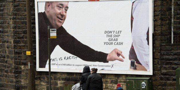 A family walk past a Conservative Party general election campaign poster featuring an image of Alex Salmond defaced with the words 'This is racist', on the eve of the general election, in Colne, northwest England, on May 6, 2015. Britain goes to the polls on May 7 to elect a new parliament. AFP PHOTO / OLI SCARFF (Photo credit should read OLI SCARFF/AFP/Getty Images)
