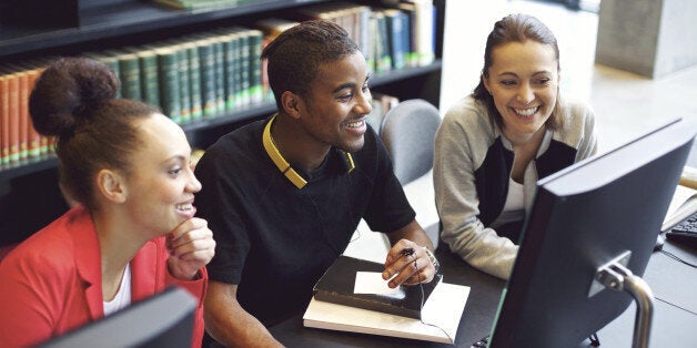 Diverse group of students using computer for finding information for their academic project. Happy young people sitting at table with books and computer taking notes for their study.