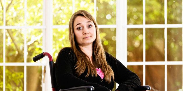 A beautiful young woman sits in her wheelchair looking resigned but mildly irritated, her eyebrows raised and shrugging, frustrated by her situation and possibly in pain.