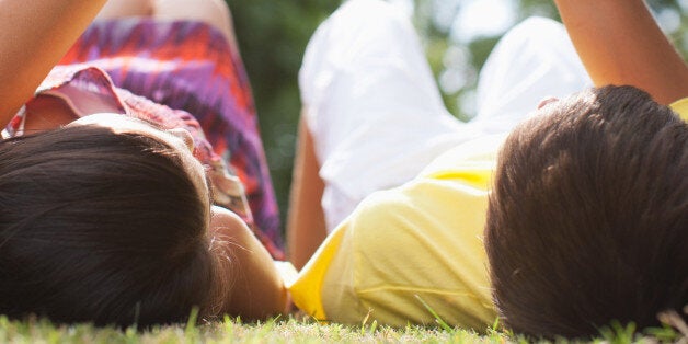 Teenagers laying in grass holding hands