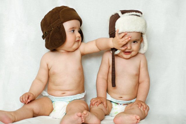Twin baby boys with diapers and hats.