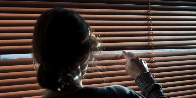 A woman looks out a window through a blind. Picture posed by model - model release available.