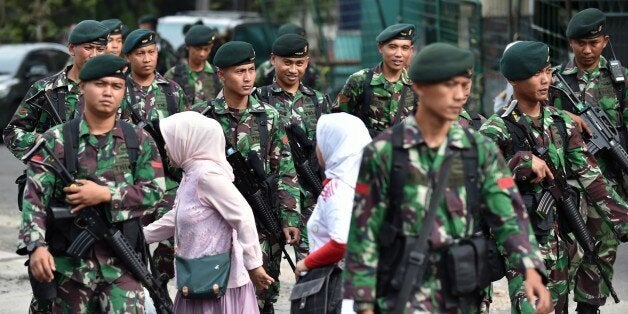 Indonesian women walk past soldiers providing security in Bandung on western Java island on April 23, 2015, ahead of a planned walk by participating heads of states scheduled for April 24 for the 60th Asian-African Conference. Asian and African leaders have gathered in Indonesia this week to mark 60 years since a landmark conference that helped forge a common identity among emerging states, but analysts say big-power rivalries will overshadow proclamations of solidarity. AFP PHOTO / Bay ISMOYO