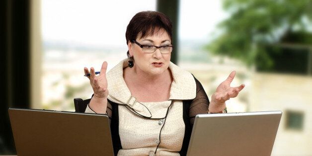 Angry glasses teacher yelling at her student during online lesson. Mature brown haired woman is looking at leptop monitor and shakes her hands