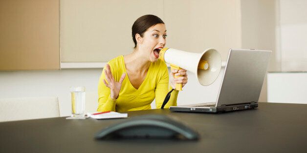 Businesswoman yelling at laptop with bullhorn in conference room